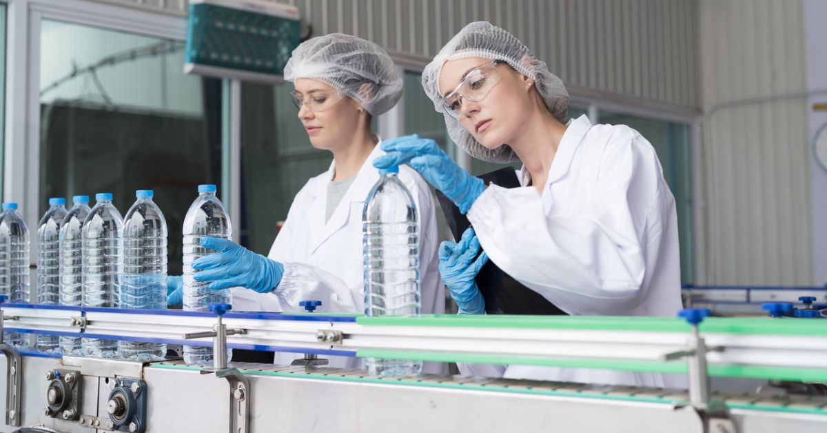Duas mulheres analisando amostras de garrafas PET com água durante o processo de controle de qualidade.