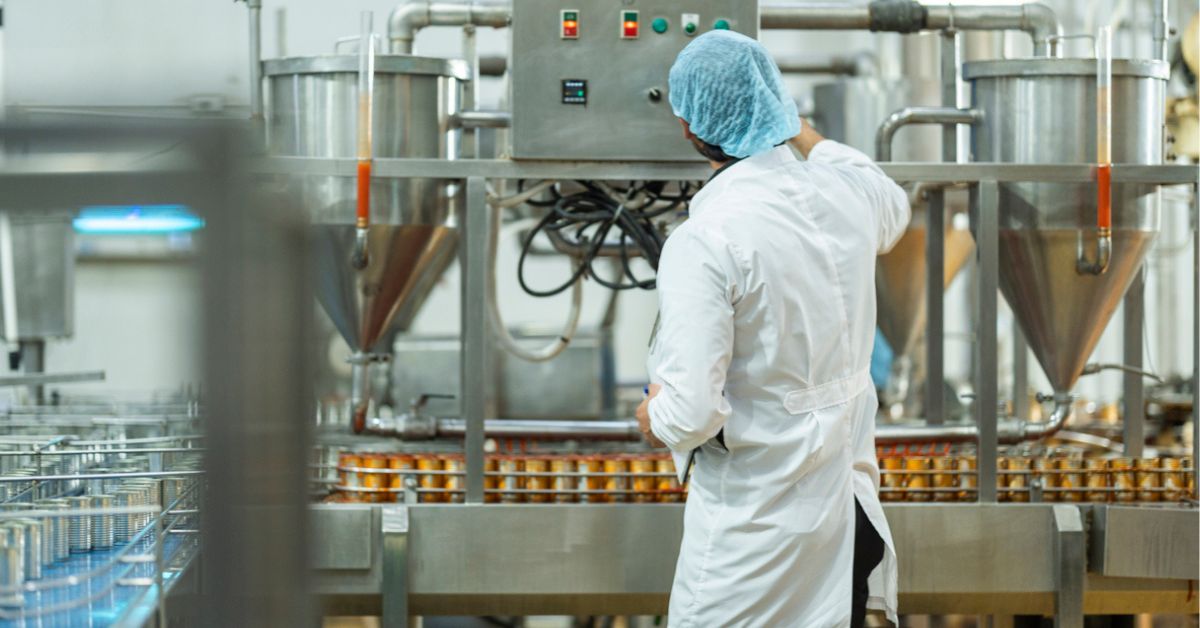 Homem vestido com roupas de proteção e higiene, operando máquina de produção em indústria alimentícia.