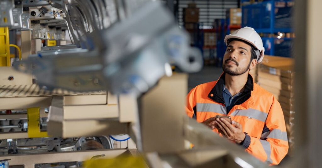 Engenheiro de Controle e Automação em frente a uma máquina industrial de metais.