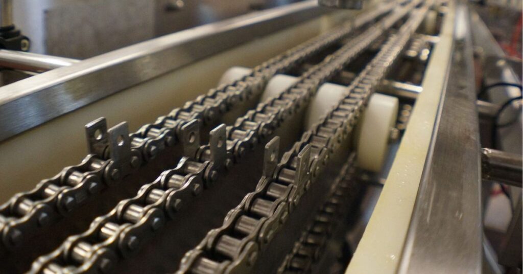 Esteira industrial de corrente com taliscas usada transporte de peças metálicas.